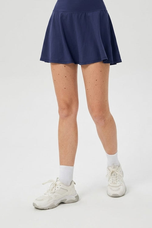 Person wearing a navy blue skirt, white sneakers, and socks on a white background