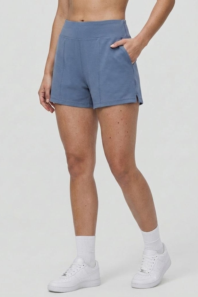Person wearing blue shorts and white sneakers on a plain background