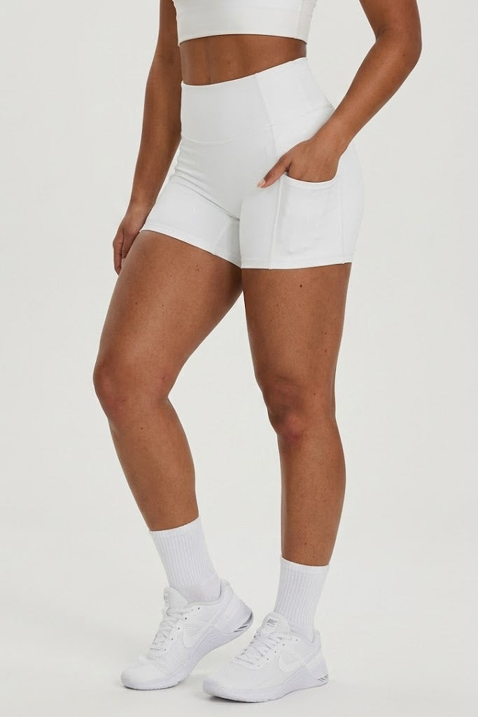 Person wearing white athletic shorts and white sneakers on a light gray background