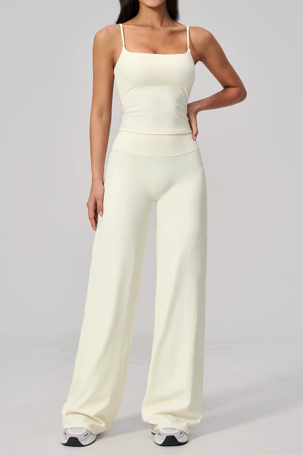 Woman wearing a white sleeveless top and wide-leg pants on a gray background