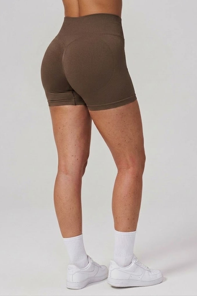 Person wearing brown shorts and white sneakers on a plain background